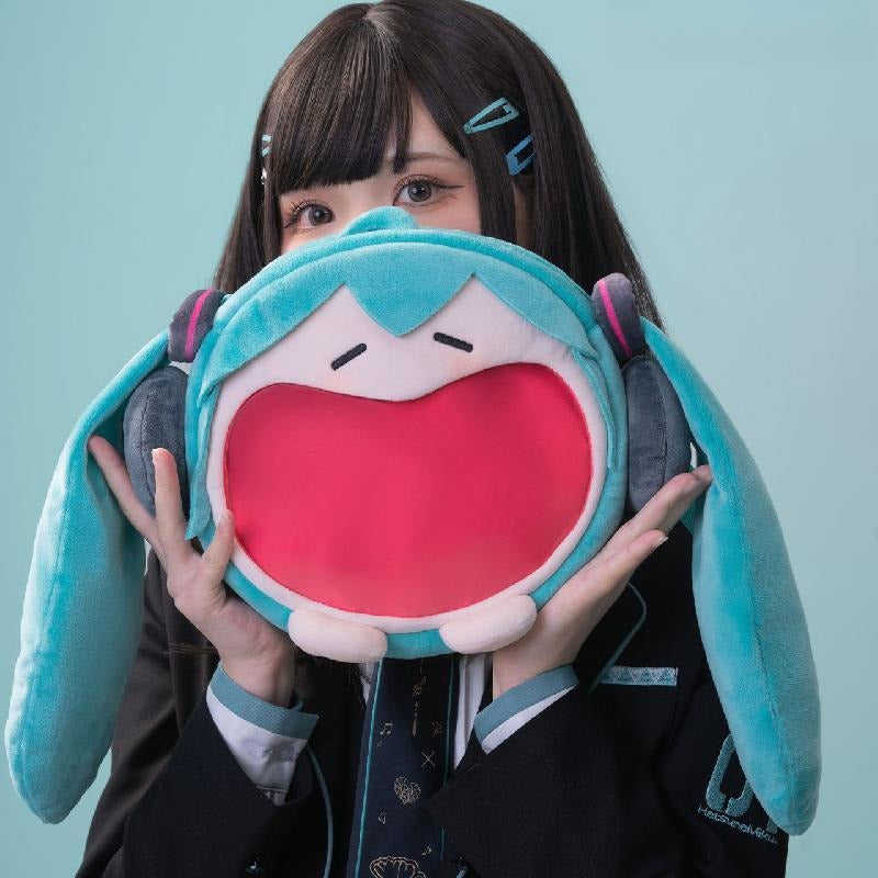 Girl in Miku uniform holding Hatsune Miku open-mouth plush bag in front of her face.