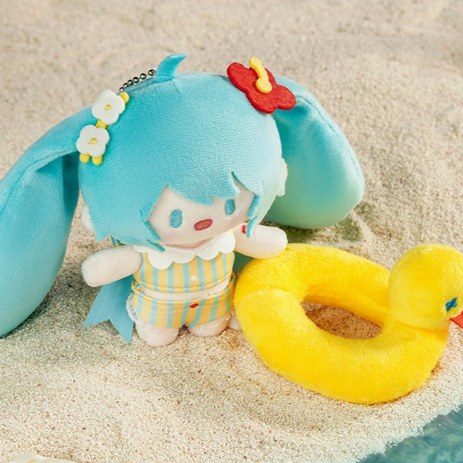 Hatsune Miku plush charm in striped swimsuit with a yellow duck, set on the sand.