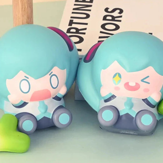 Two chibi Hatsune Miku squishy toys with exaggerated facial expressions on a pastel desk