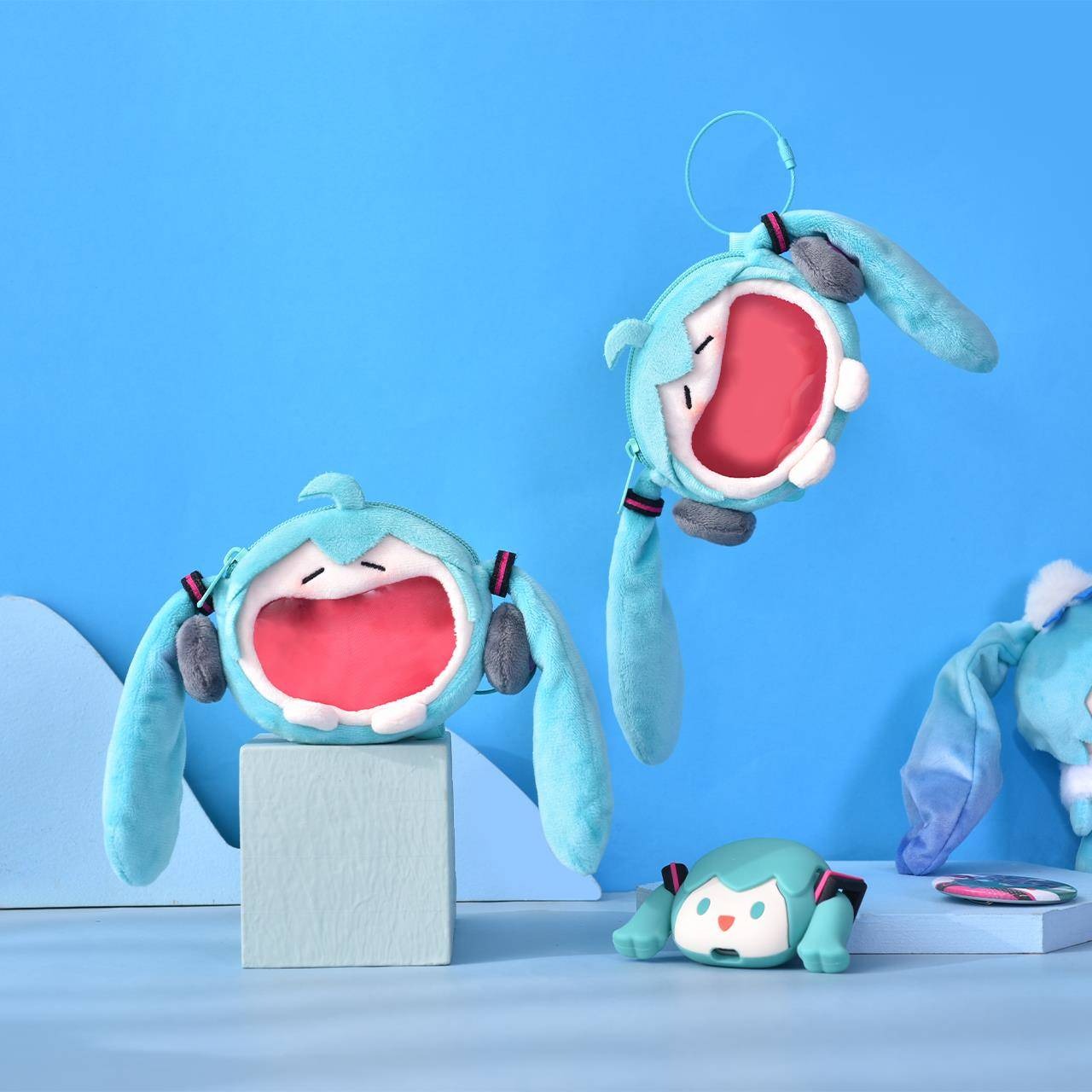 Multiple Hatsune Miku plush coin pouches with open-mouth design and twin tails on blue setup.