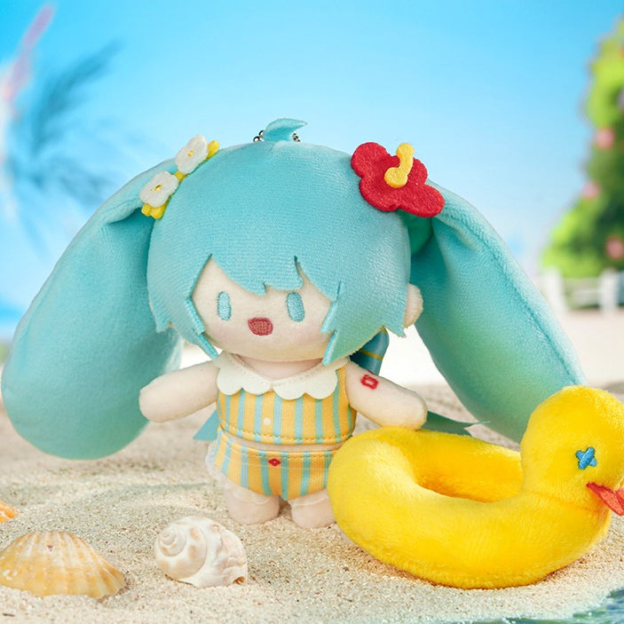 Hatsune Miku plush charm in striped swimsuit with yellow duck, placed on the sandy beach